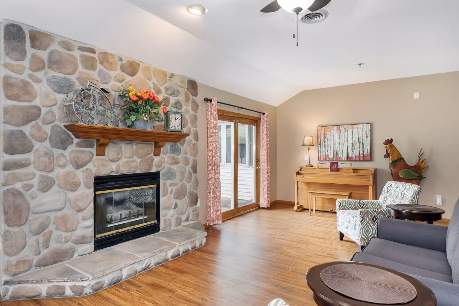 Cozy living room with a stone fireplace, hardwood floors, seating, a piano, and sliding glass doors.