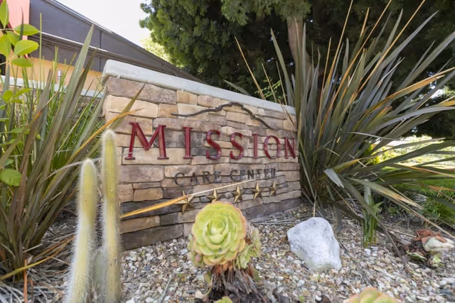 A stone entrance sign reading 'MISSION CARE CENTER' set among succulents and landscaping.