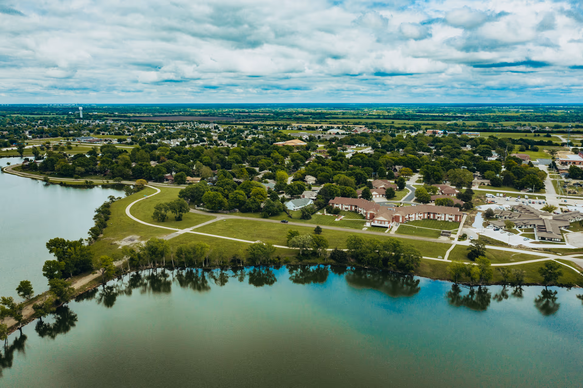 Aerial view of a lakeside senior living campus with buildings, walking paths, trees, and a large body of water.