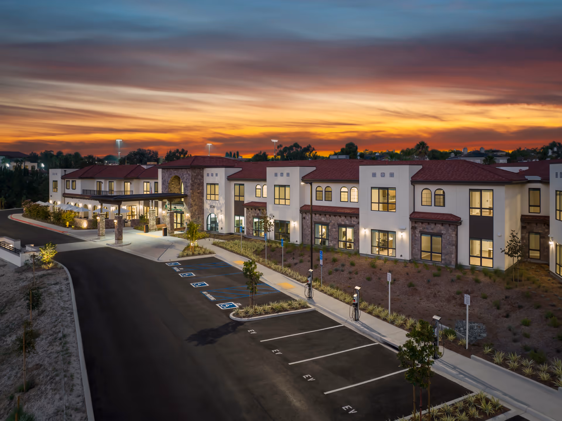 Exterior evening view of the Westmont of Carmel Valley building with lit windows, a covered entrance, and an empty parking lot under a colorful sunset.