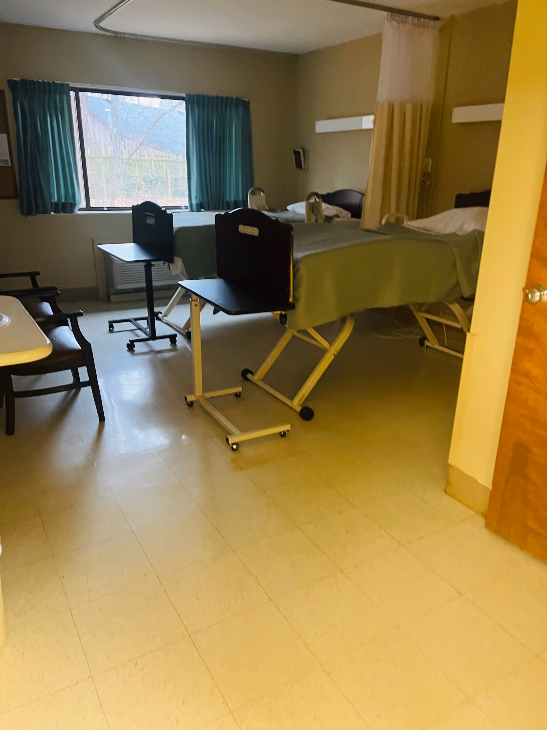 Empty patient room with two beds, curtains, window, and medical equipment.