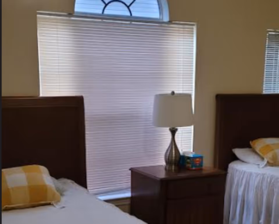 Two twin beds with a nightstand and lamp in a bright bedroom.