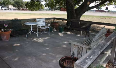 Outdoor patio at Leonard Manor with chairs, table, tree, and potted plants.