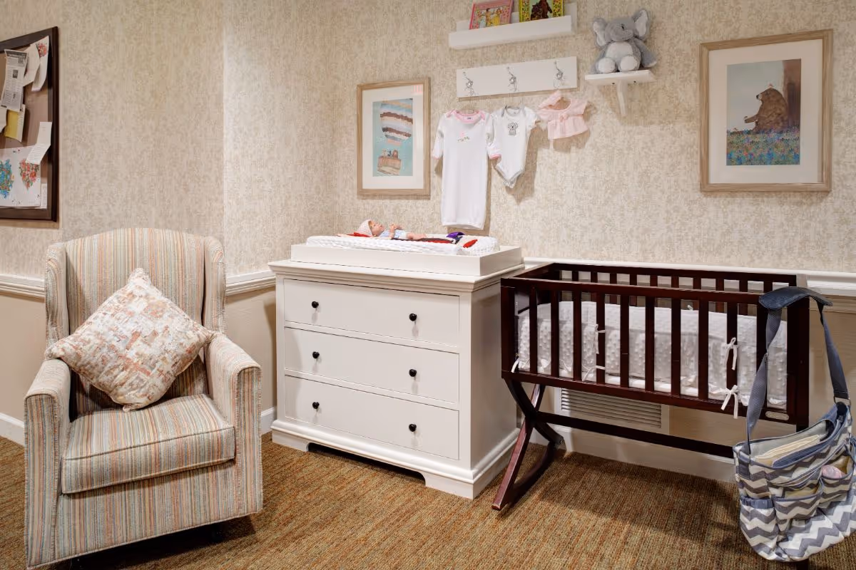 Cozy nursery corner with an upholstered armchair, a white changing dresser with a changing pad, and a dark wooden baby crib.