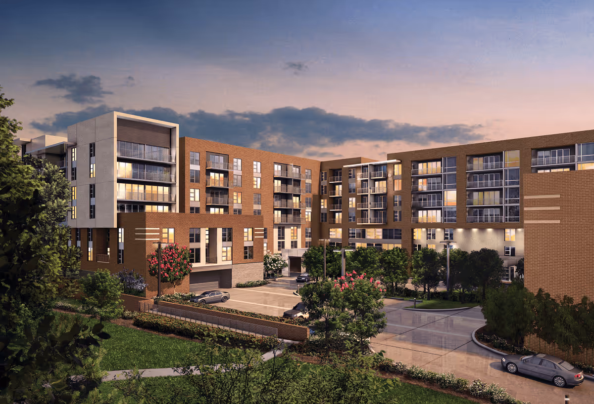 Exterior view of a modern multi-story senior living facility building at dusk with large windows, balconies, landscaped greenery, trees, and parked cars in the driveway.