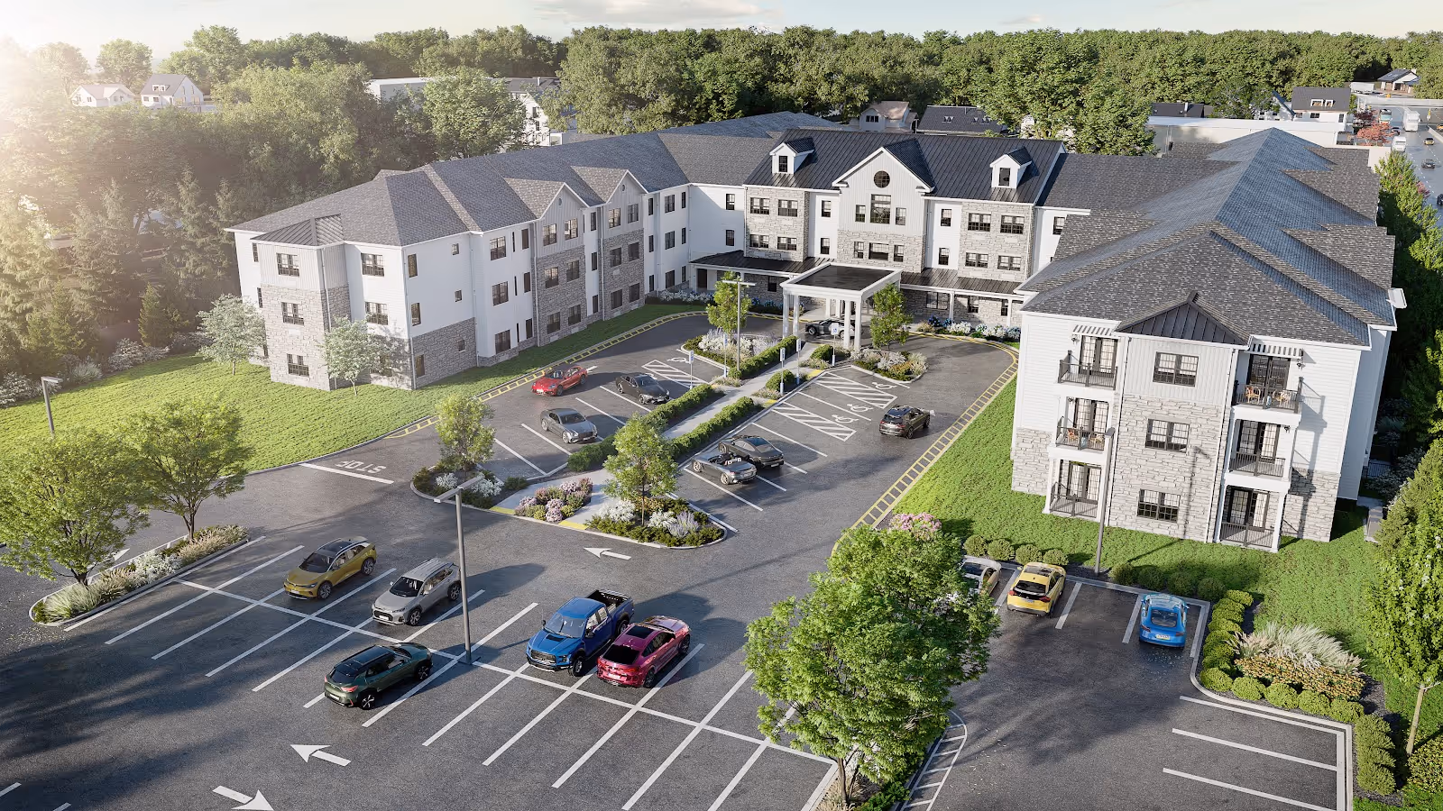 Aerial view of a three-story senior living building with a covered entrance, parking lot, and landscaped grounds surrounded by trees.