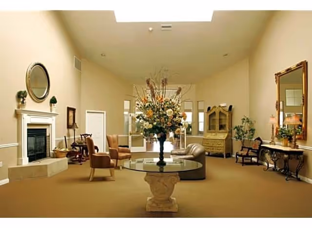 Spacious furnished sitting room/lobby with a central round table holding a large floral arrangement, multiple seating areas, a fireplace, and a skylight.