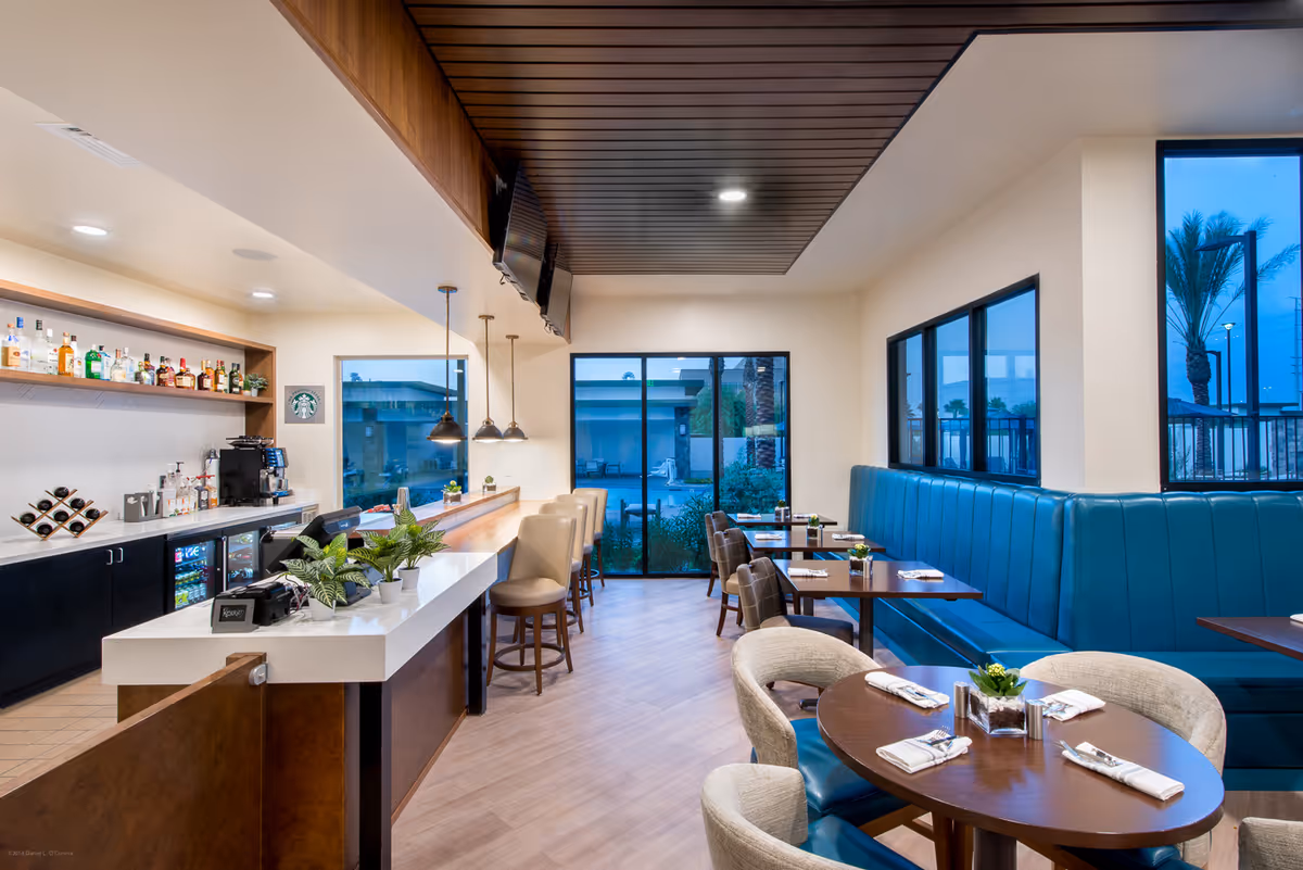 Modern dining room with a bar and counter seating, teal banquette booths and round tables set for dining.