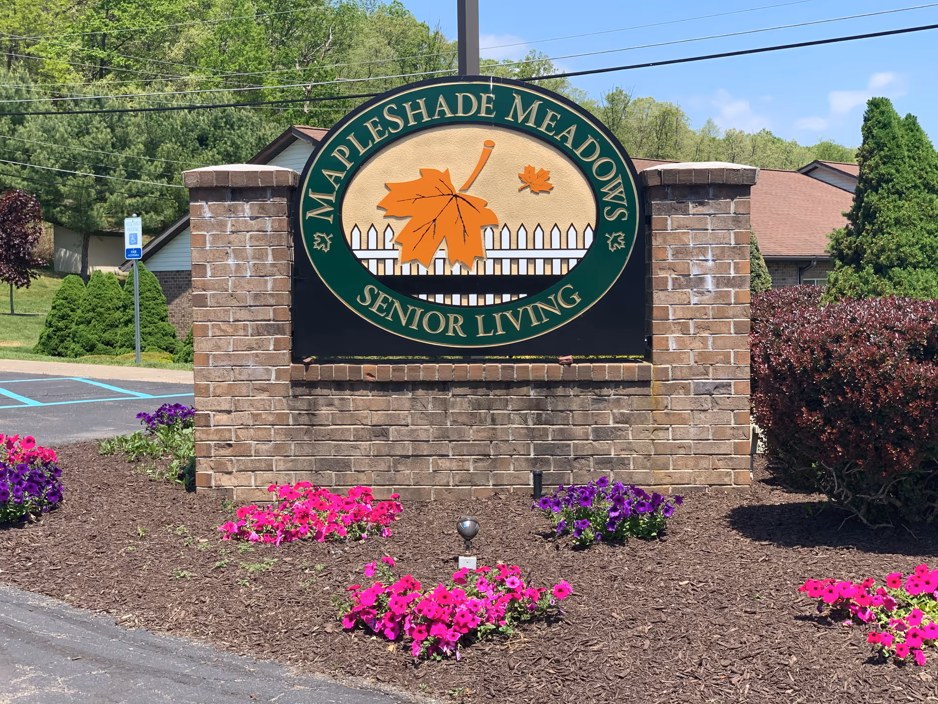 Brick entrance sign for Mapleshade Meadows Senior Living surrounded by flower beds, shrubs, and a building in the background.