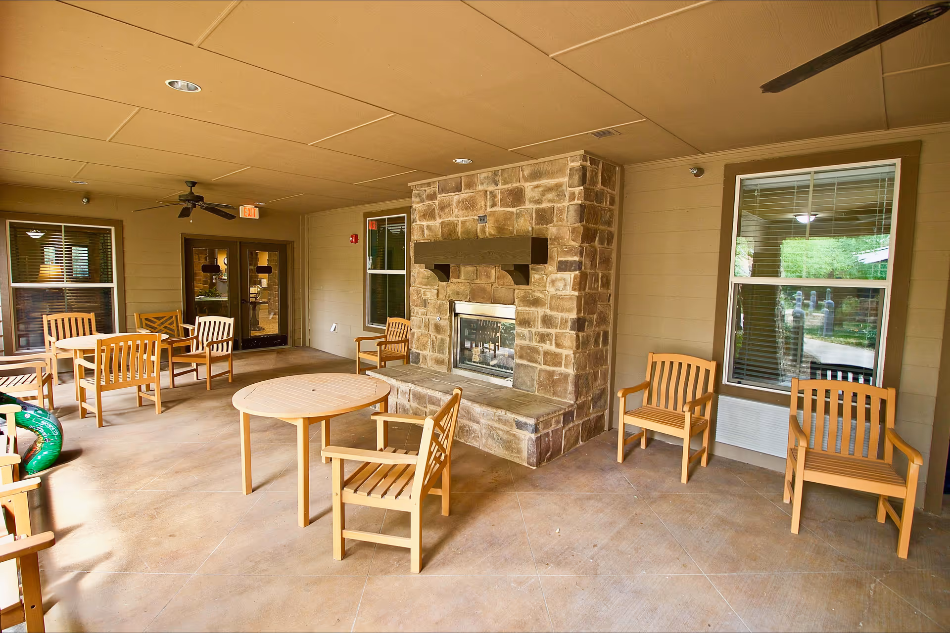 Covered common room with a stone fireplace surrounded by wooden chairs and round tables.