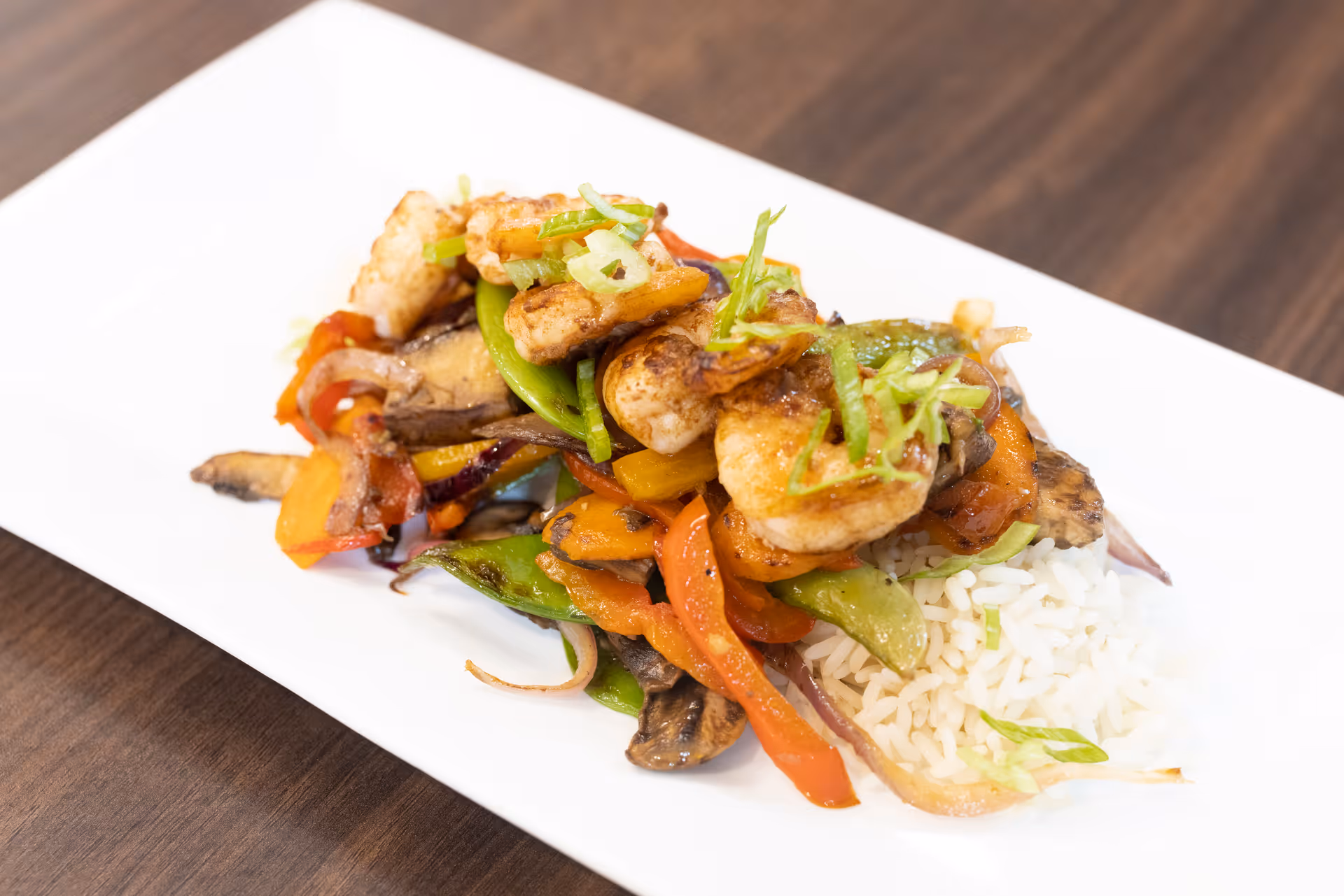 A plated shrimp and vegetable stir-fry served with rice on a rectangular white plate.