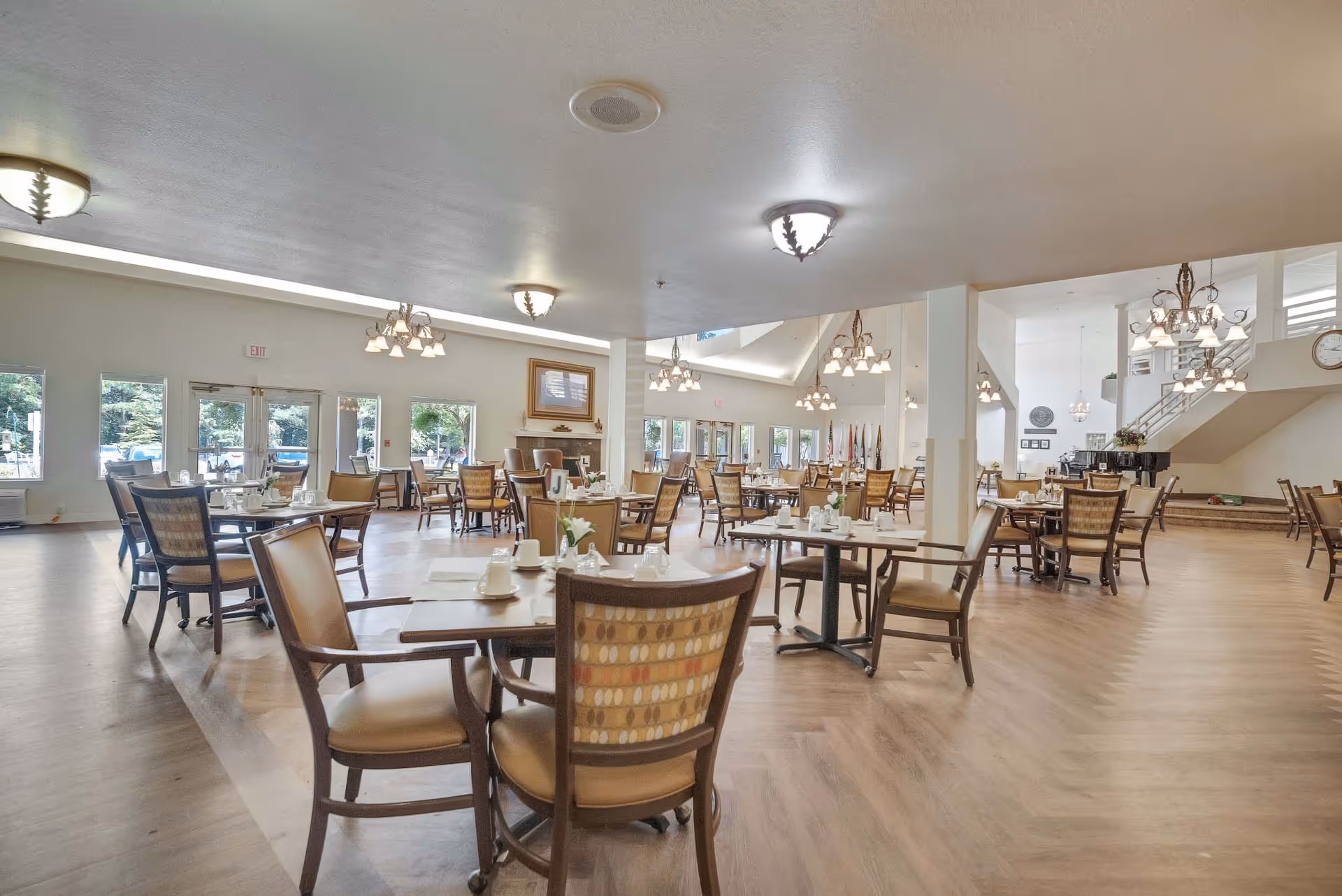 Spacious bright dining room with multiple set dining tables and chairs, chandeliers, and large windows.