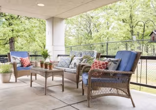 Covered outdoor patio with wicker sofa and chairs, a coffee table with potted plants, and cushions overlooking trees.