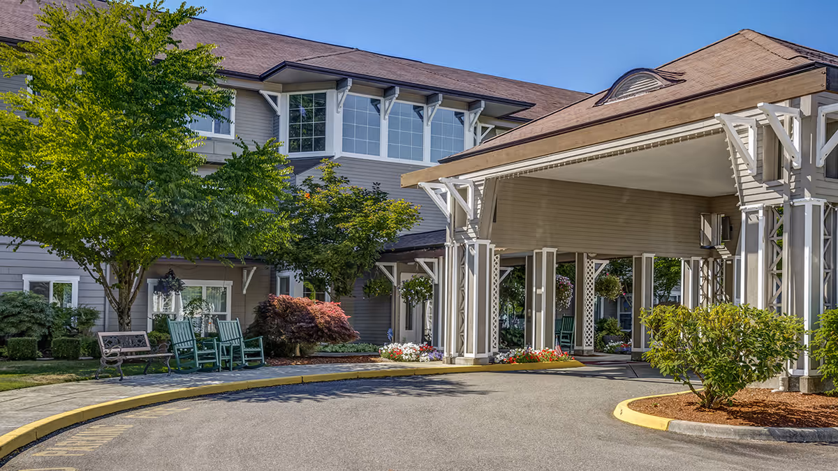 Covered porte-cochère entrance of a multi-story senior living building with landscaping and outdoor seating.