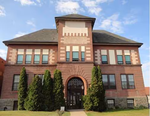 Front view of a brick senior living residence with arched entry and tall trees.