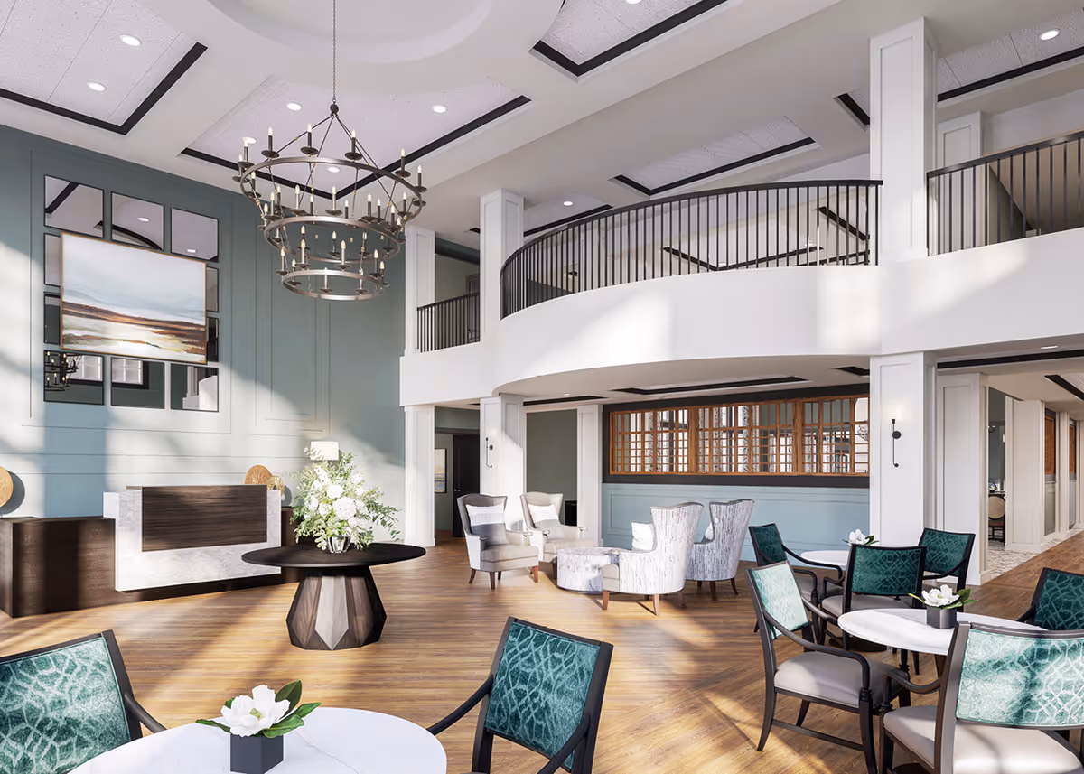 A spacious and well-lit senior living facility common area with high ceilings, a large chandelier, multiple seating arrangements including armchairs and tables with green cushioned chairs, a central round table with a floral arrangement, and a reception desk against a light green wall with a large landscape painting.