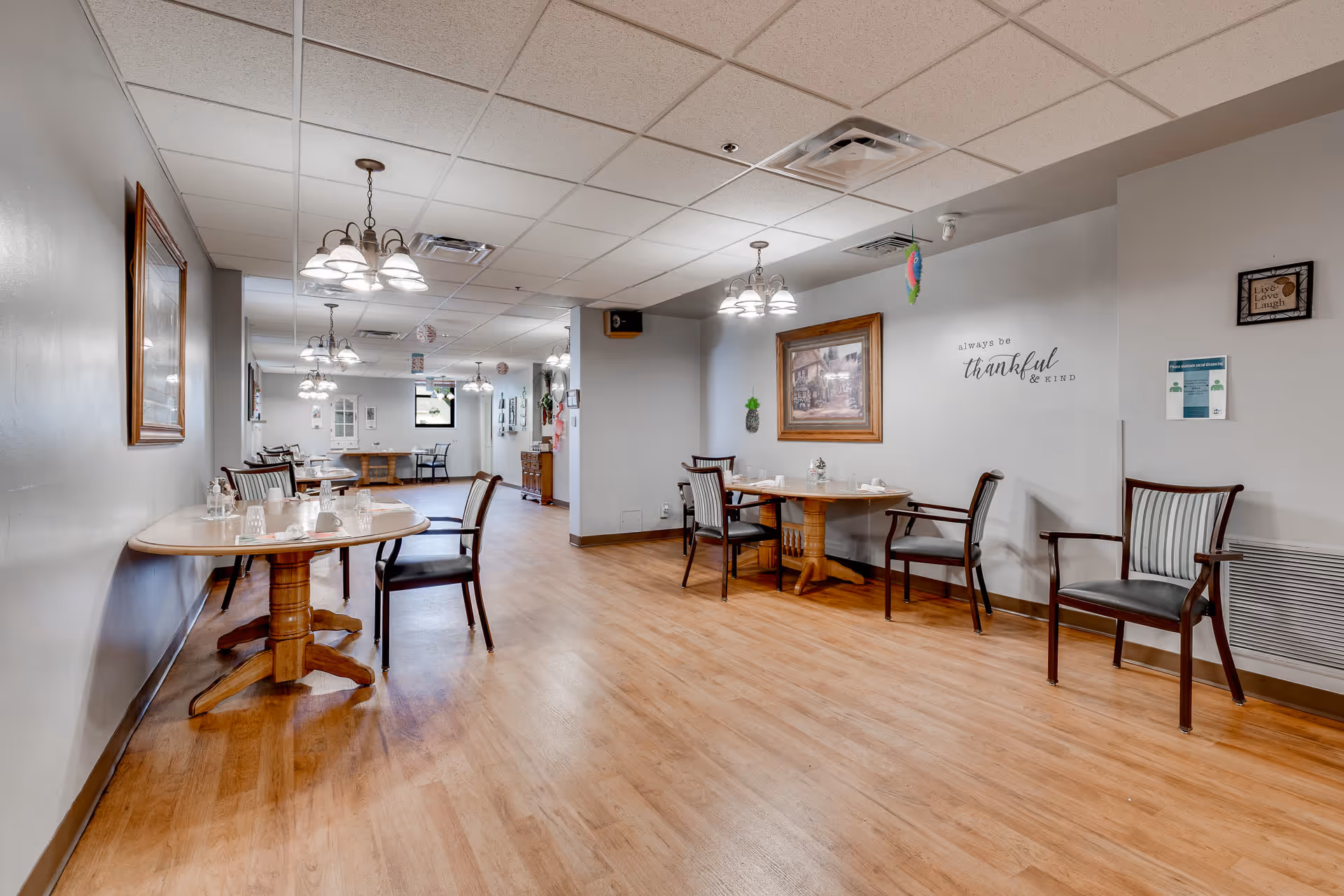 Spacious dining room with wooden tables and chairs set for meals, wall art, and overhead lighting.