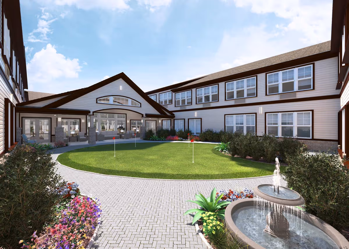 Landscaped courtyard with a small putting green, fountain, flower beds and seating surrounded by a two-story senior living building.