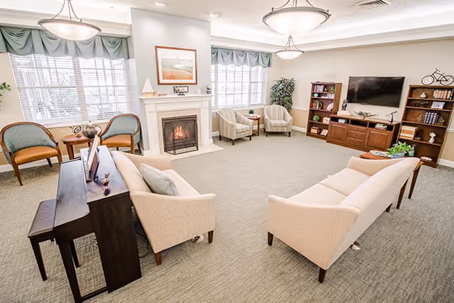 Bright communal living room with sofas, a fireplace, a TV and bookshelves near large windows.