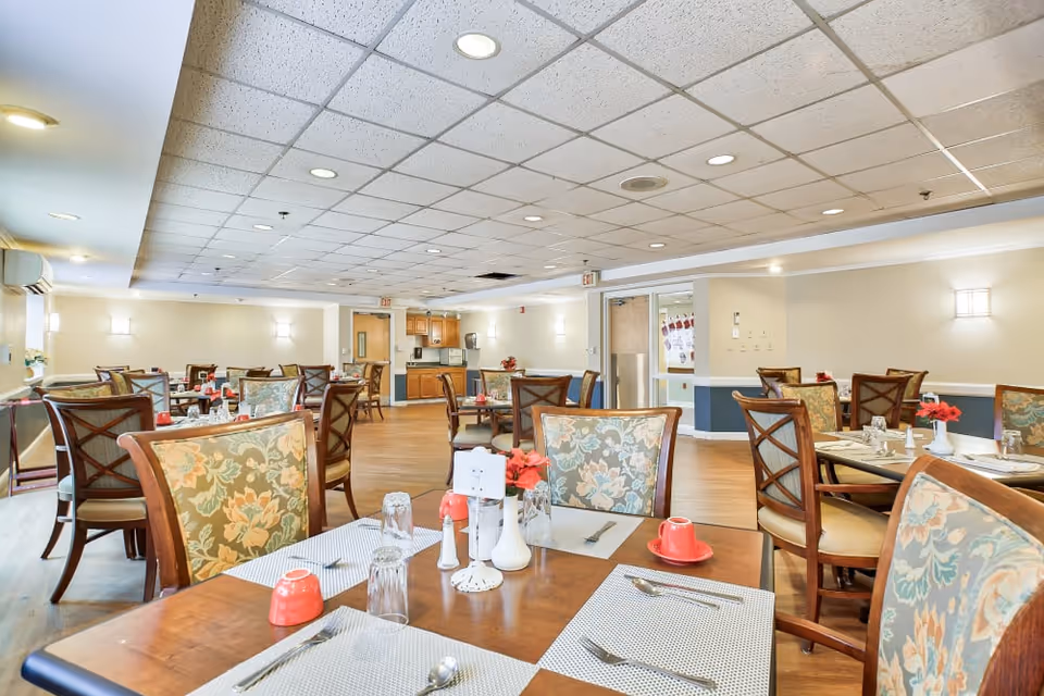 Bright dining room with multiple set tables and floral-upholstered chairs and place settings.