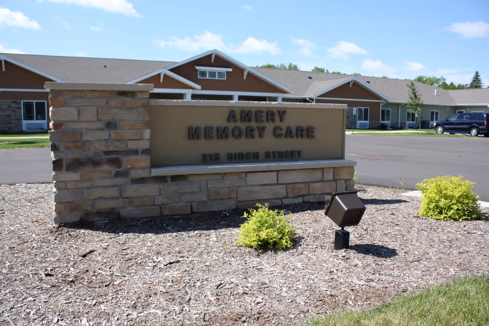 Stone sign displaying Amery Memory Care in front of a single-story building with landscaping