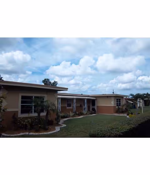 Single-story facility exterior with landscaped lawn, shrubs, and large windows.