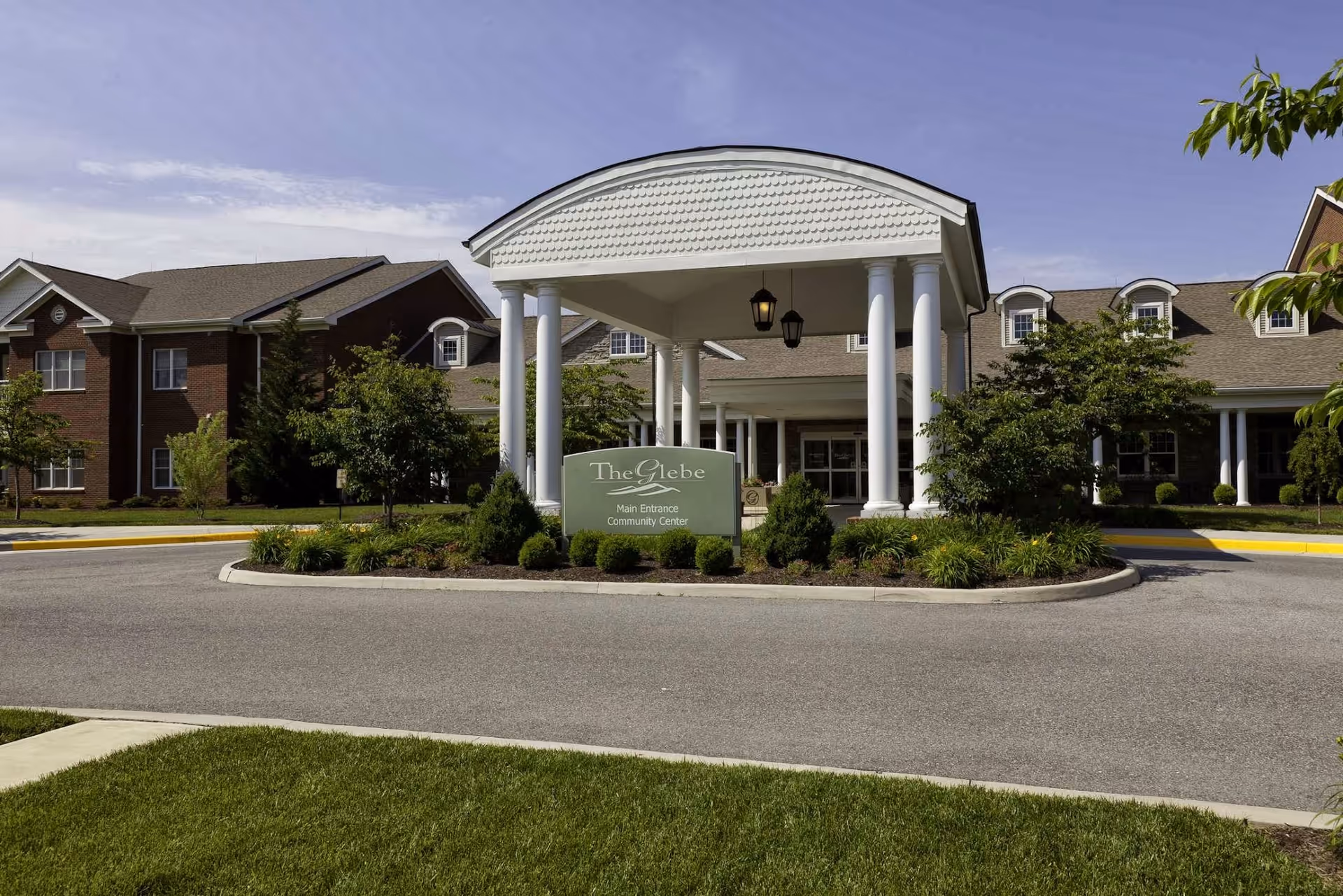 Front entrance of The Glebe Retirement Community with a columned porte-cochere, sign, and landscaped driveway.
