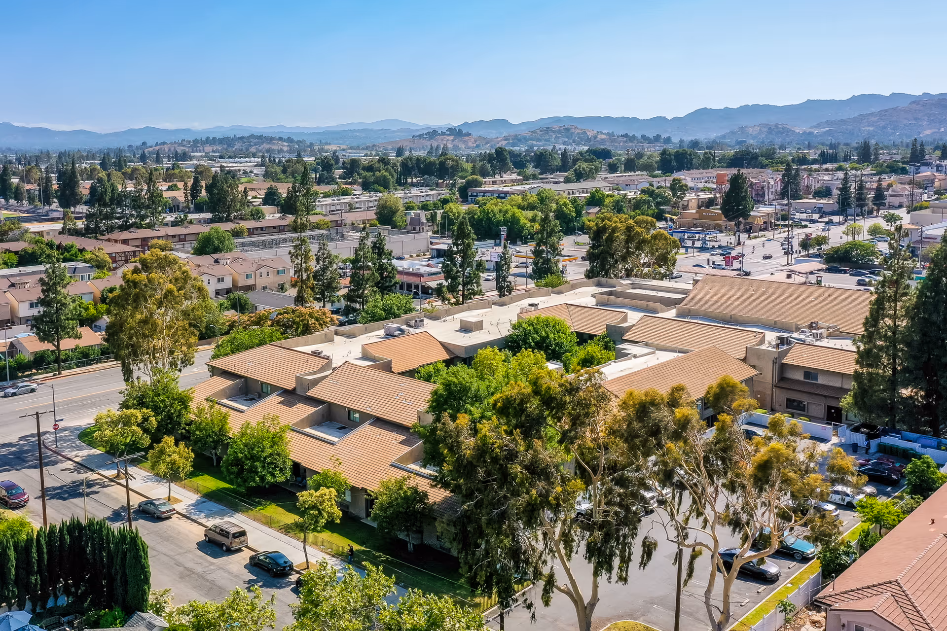 Aerial view of Brookdale Chatsworth senior living facility surrounded by trees and residential buildings, with mountains visible in the background under a clear blue sky.