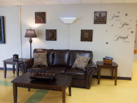 Cozy senior living lounge with leather sofa, wooden coffee tables, and wall art.