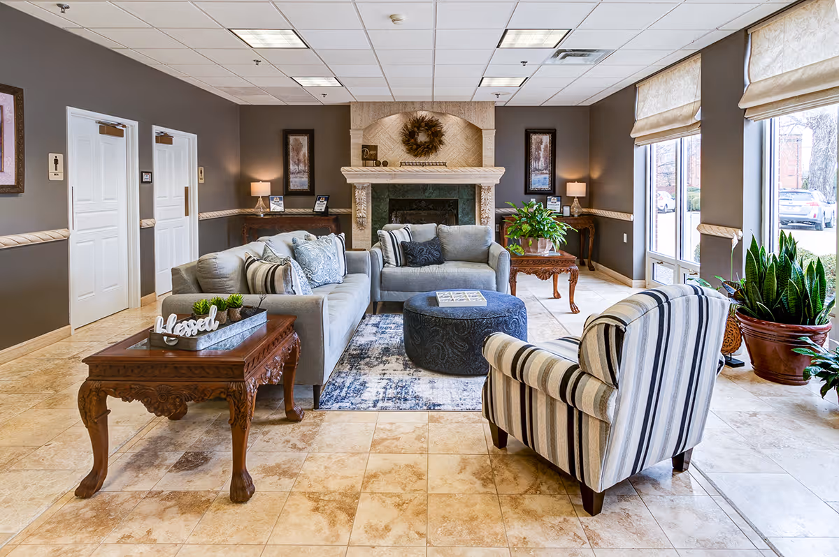 Bright, furnished lounge with sofas, a striped armchair, coffee tables, a fireplace, and large windows.