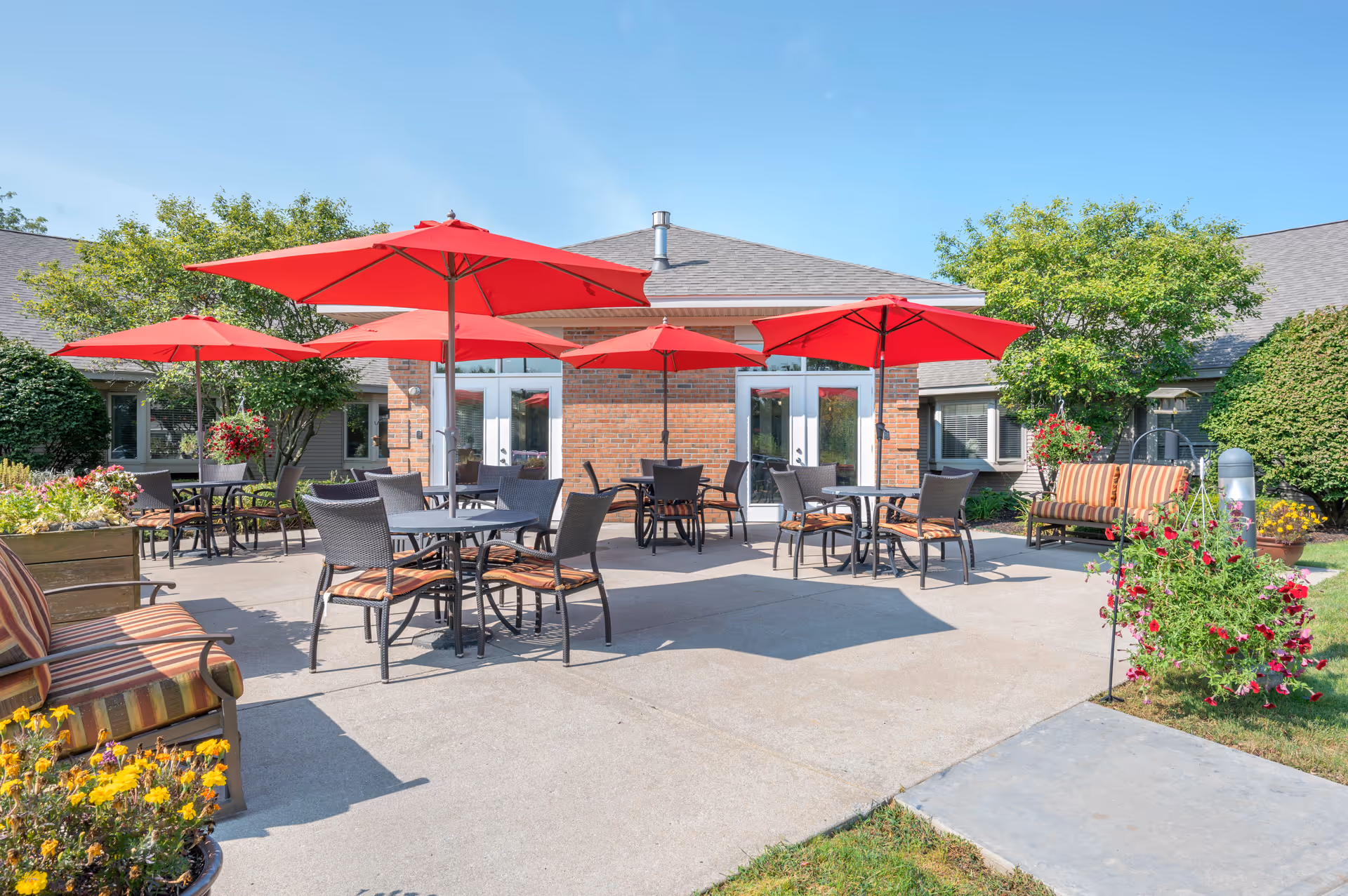 Outdoor patio with red umbrellas, tables, and chairs in front of a brick building
