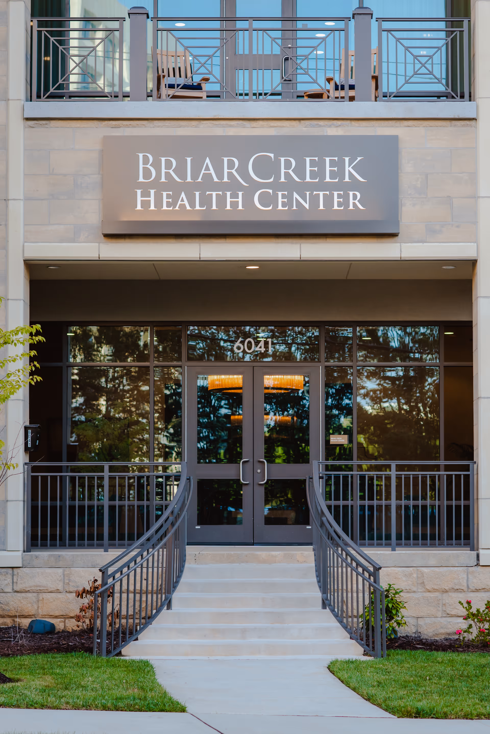 Front entrance of Briar Creek Health Center showing a large sign above double glass doors with steps and metal railings leading up.
