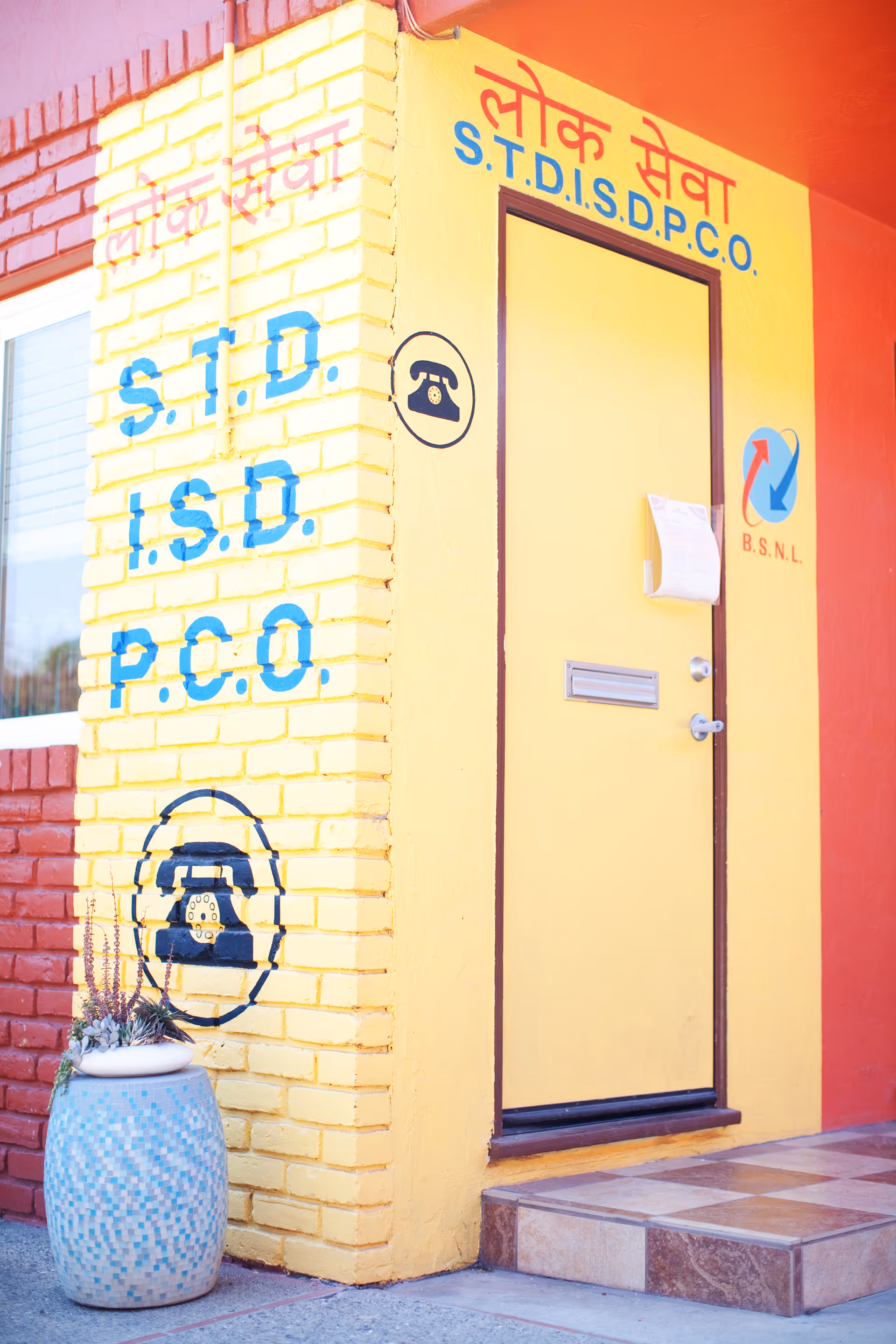 Yellow and red storefront entrance with a yellow door and painted signage reading S.T.D., I.S.D., P.C.O. and phone symbols.