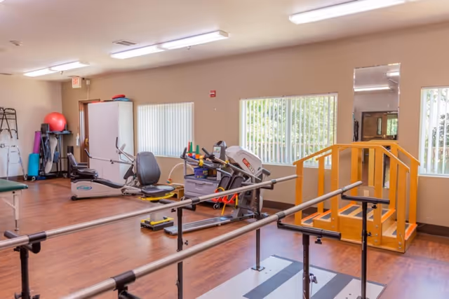 Rehabilitation gym with parallel bars, exercise machines, and a wooden step ramp in a bright room.