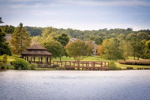Lakeside park with gazebo, wooden pier, and grassy trees in the background.