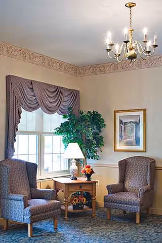 Two upholstered chairs flank a small table with lamp and flowers in a cozy living room.