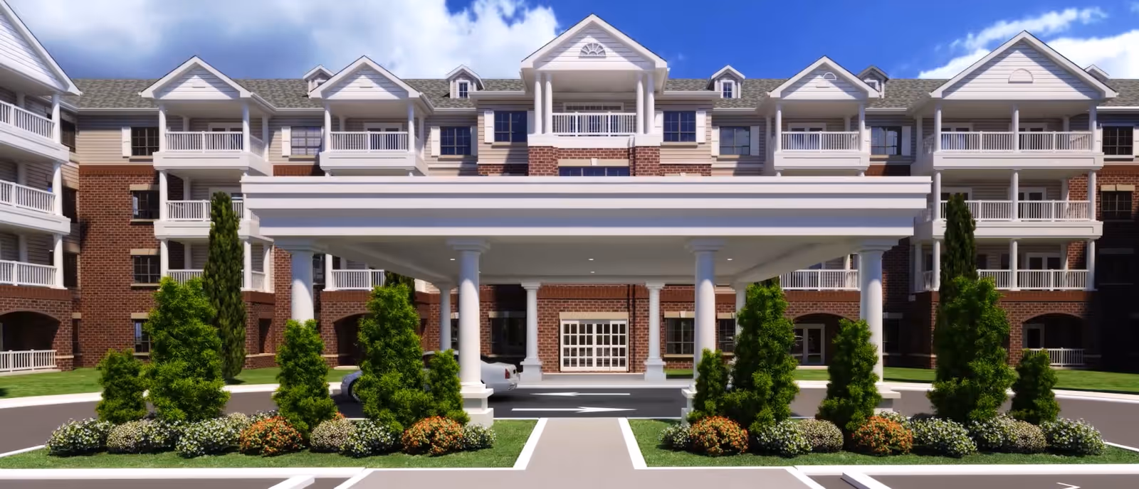 Front exterior view of a large senior living facility named Harmony at Enterprise, featuring a covered entrance with white columns, multiple balconies, brick and siding facade, landscaped greenery, and a clear blue sky.