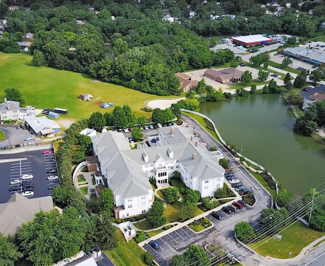 Aerial view of The Summit of Edgewood senior living complex by a pond with parking lots and surrounding trees and lawns.