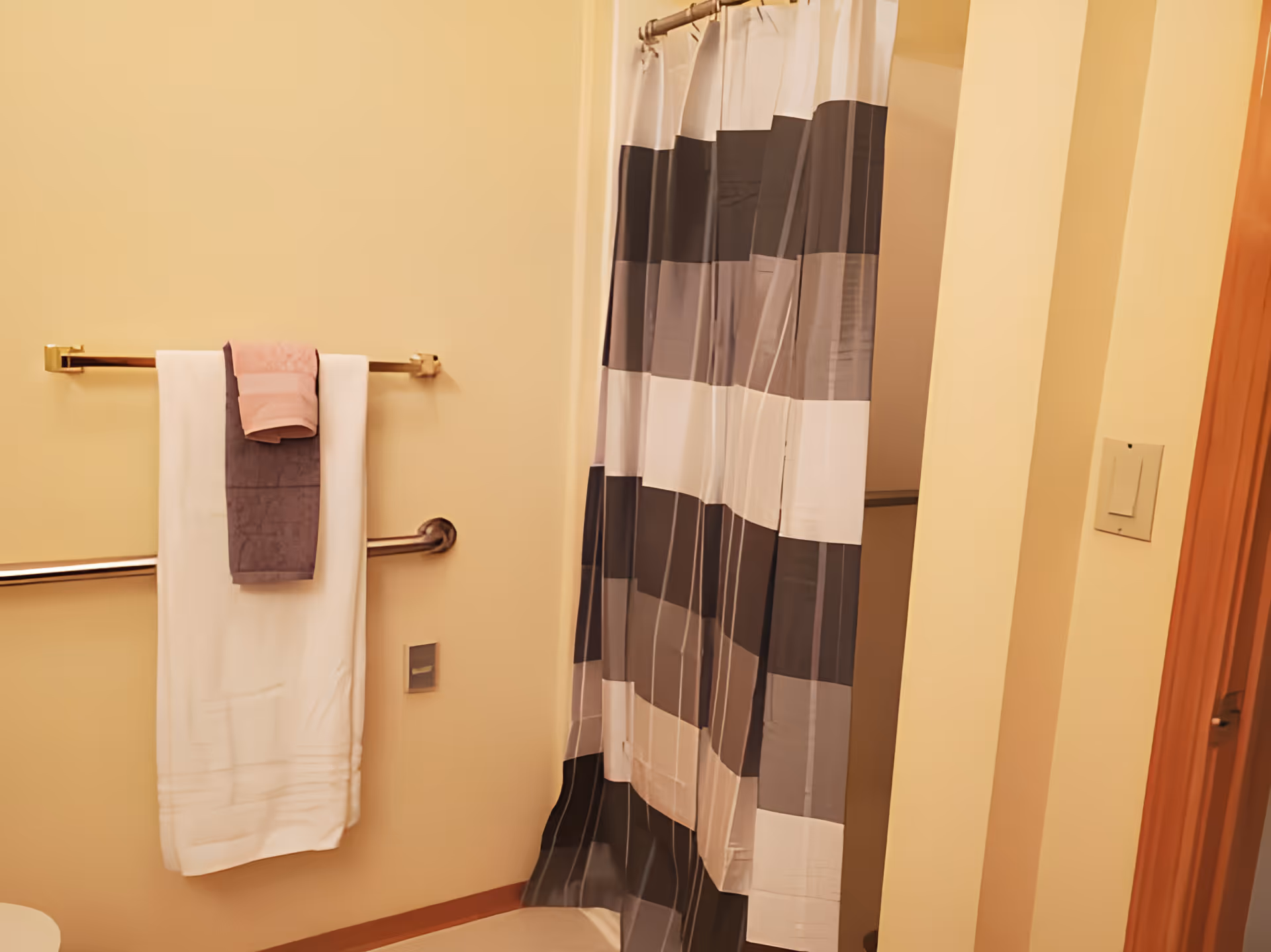 Bathroom interior showing a shower with a striped curtain, a towel rack with folded towels, and a safety grab bar.