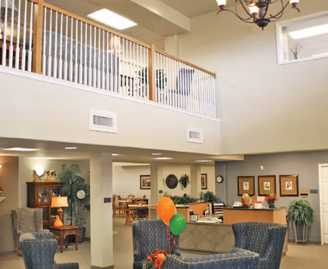 Two-story senior living facility lobby with seating areas, a reception desk, and colorful balloons.