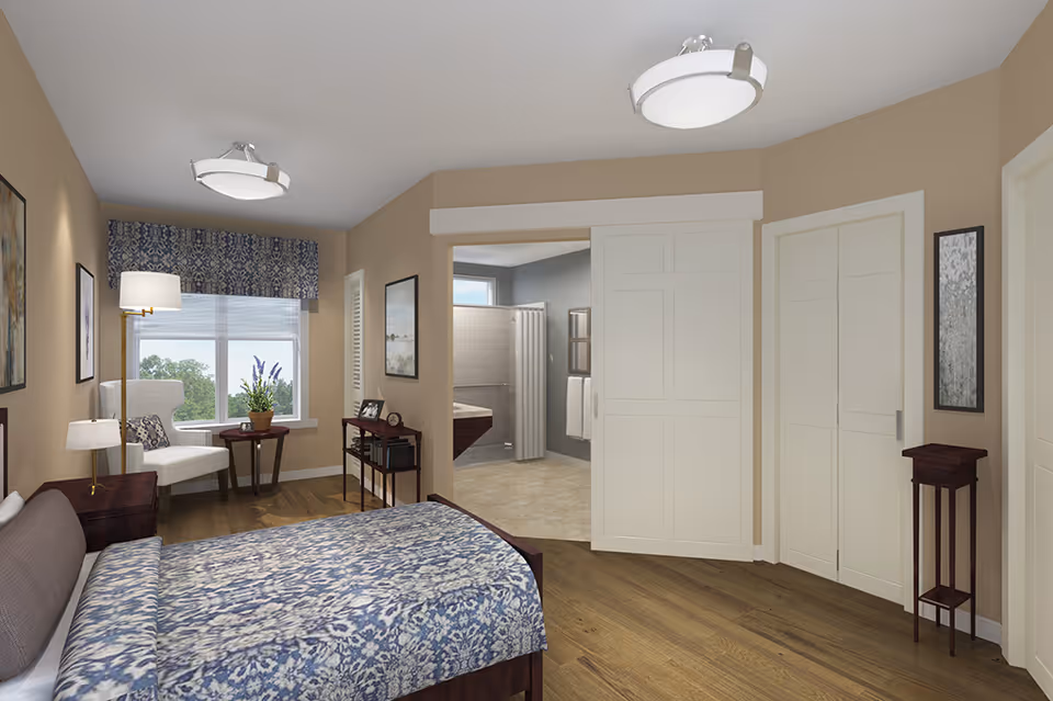 A cozy bedroom with a bed covered in a blue and white patterned bedspread, a white armchair next to a window with a floral valance, a small wooden table with a potted plant, and a wooden floor. The room has beige walls and two ceiling lights. There is an open sliding door leading to a bathroom with a shower and a sink.