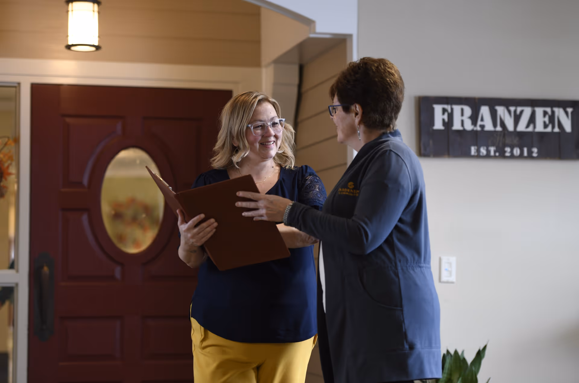 Two people talking in a facility lobby near a red door, one holding a folder.