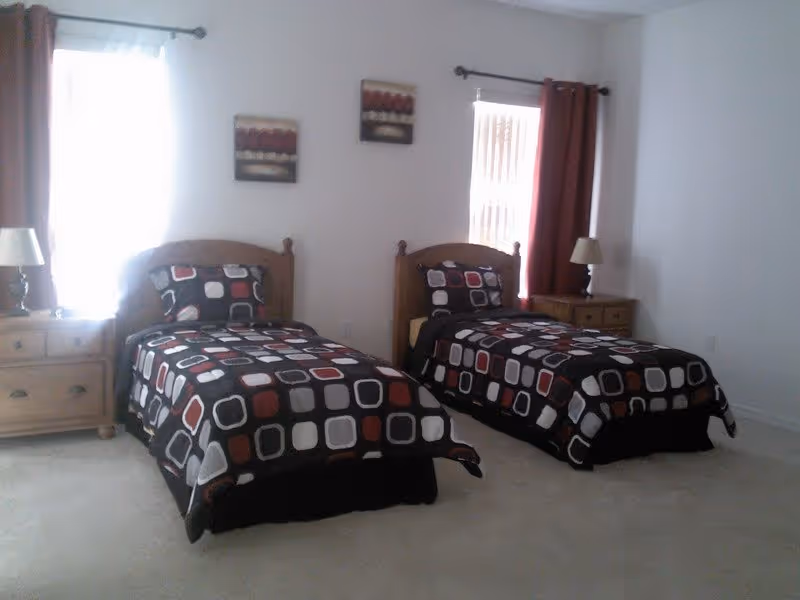 Bright bedroom with two twin beds featuring black, white, and red patterned bedding, wooden headboards, nightstands, and lamps.