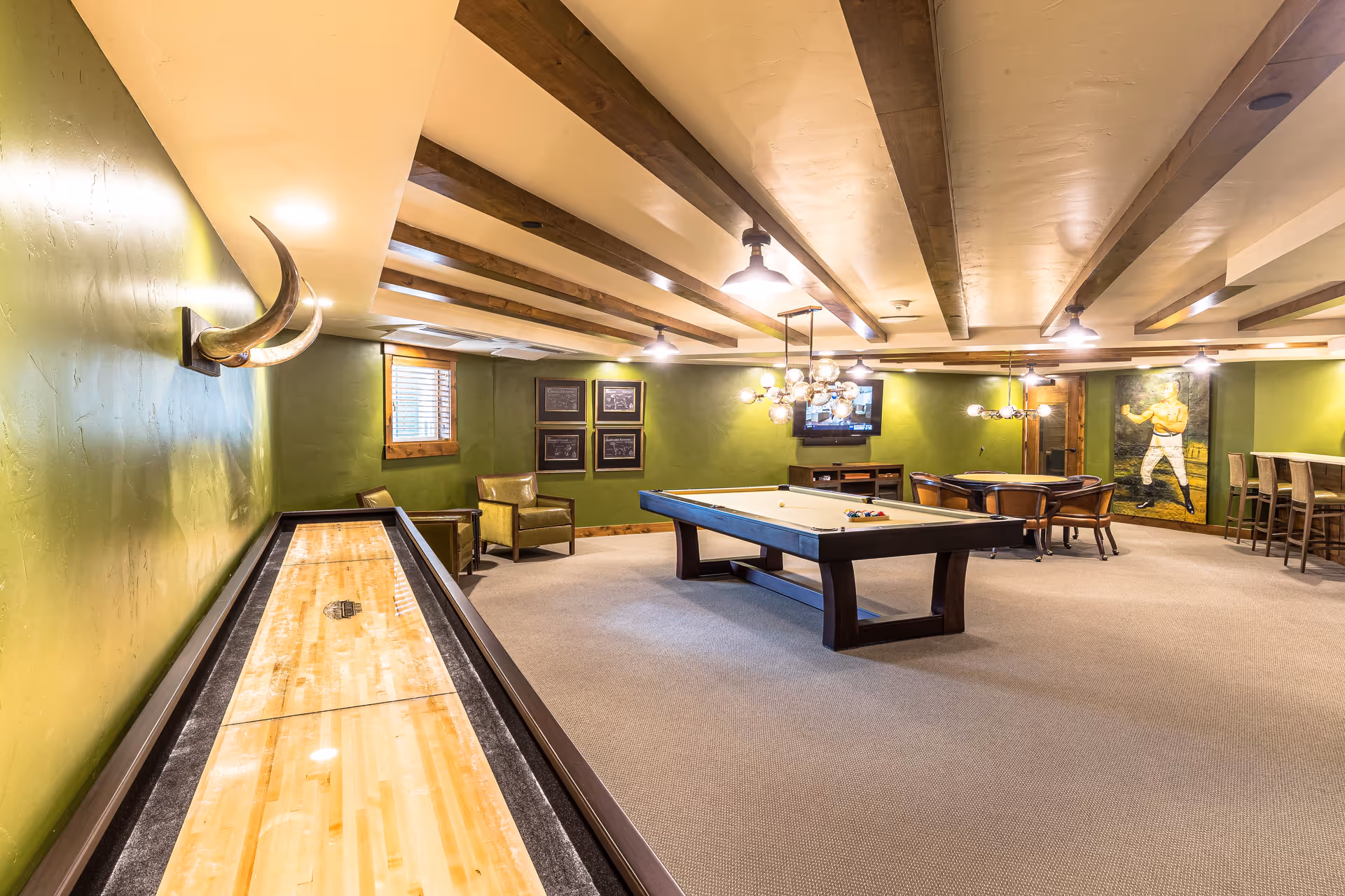 Spacious green-walled game room with a pool table, shuffleboard, seating, bar stools, and a wall-mounted TV.