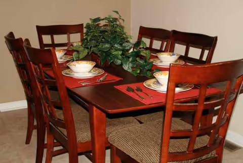 Dining room table set for six with bowls, napkins, and a leafy centerpiece.