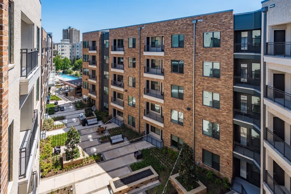 View of a landscaped central courtyard with seating, balconies and a pool area between multi-story brick apartment buildings.