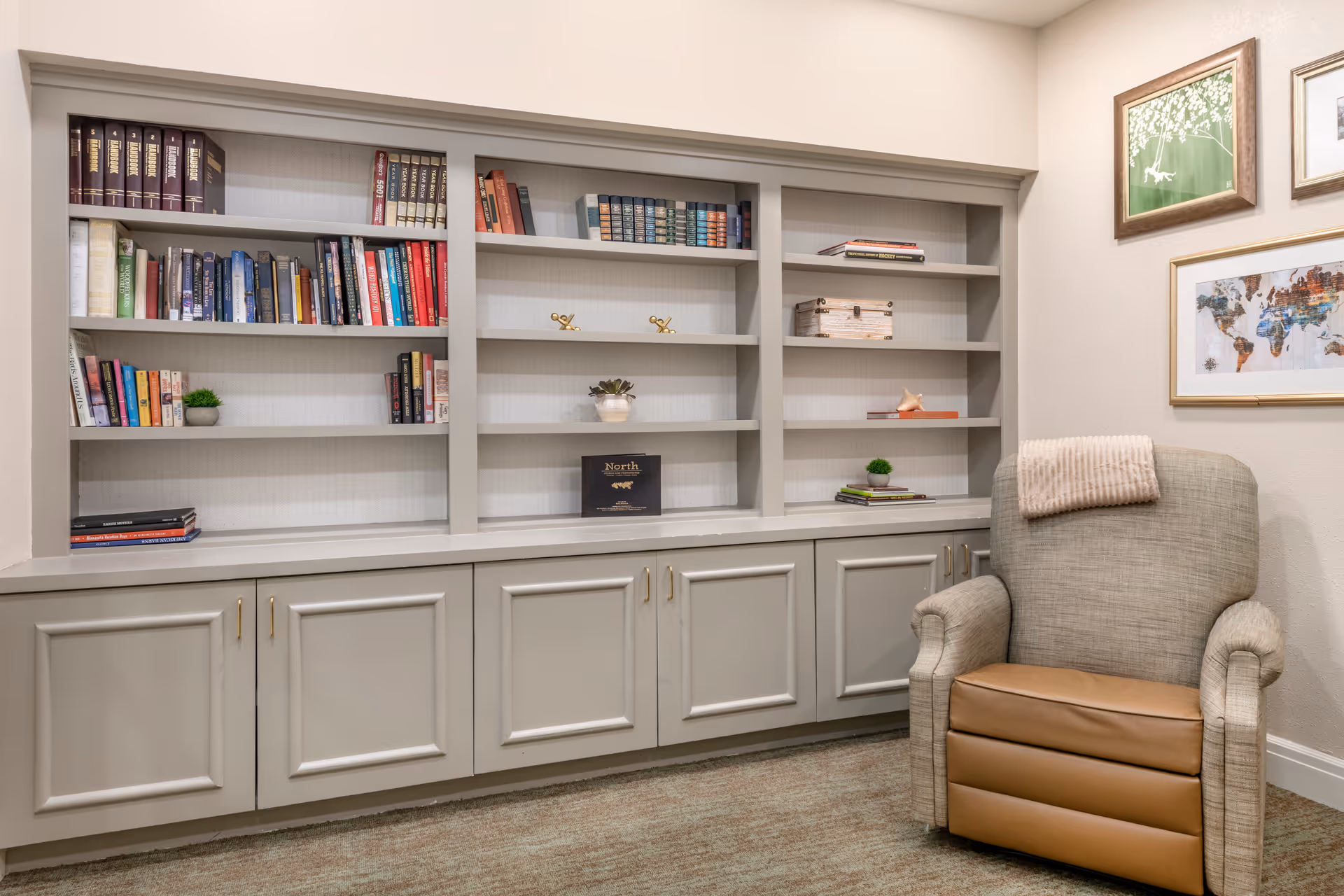Built-in bookshelves and lower cabinets beside a comfortable upholstered armchair in a cozy reading nook.