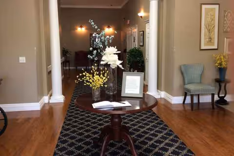 Lobby seating area with a round table, flowers, framed document, and decorative art.