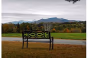 Outdoor park bench with autumn trees and distant mountains in the background.