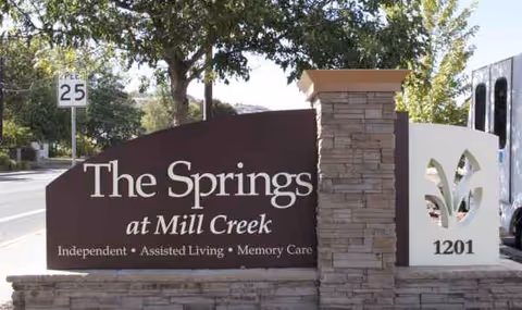 Front exterior sign reads The Springs at Mill Creek with stone pillar and roadway nearby.